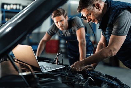 Car repairmen using laptop while doing car engine diagnostic in auto repair shop